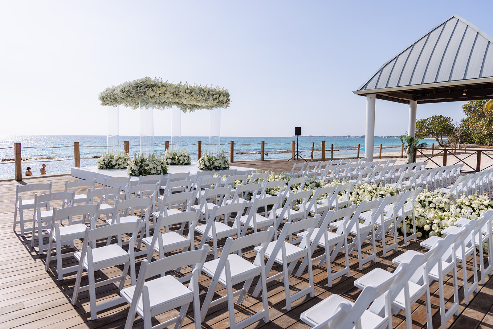 Luxury white destination wedding ceremony in Grand Cayman featuring an acrylic floral chuppah and ocean views, designed by Celebrations Weddings & Events.