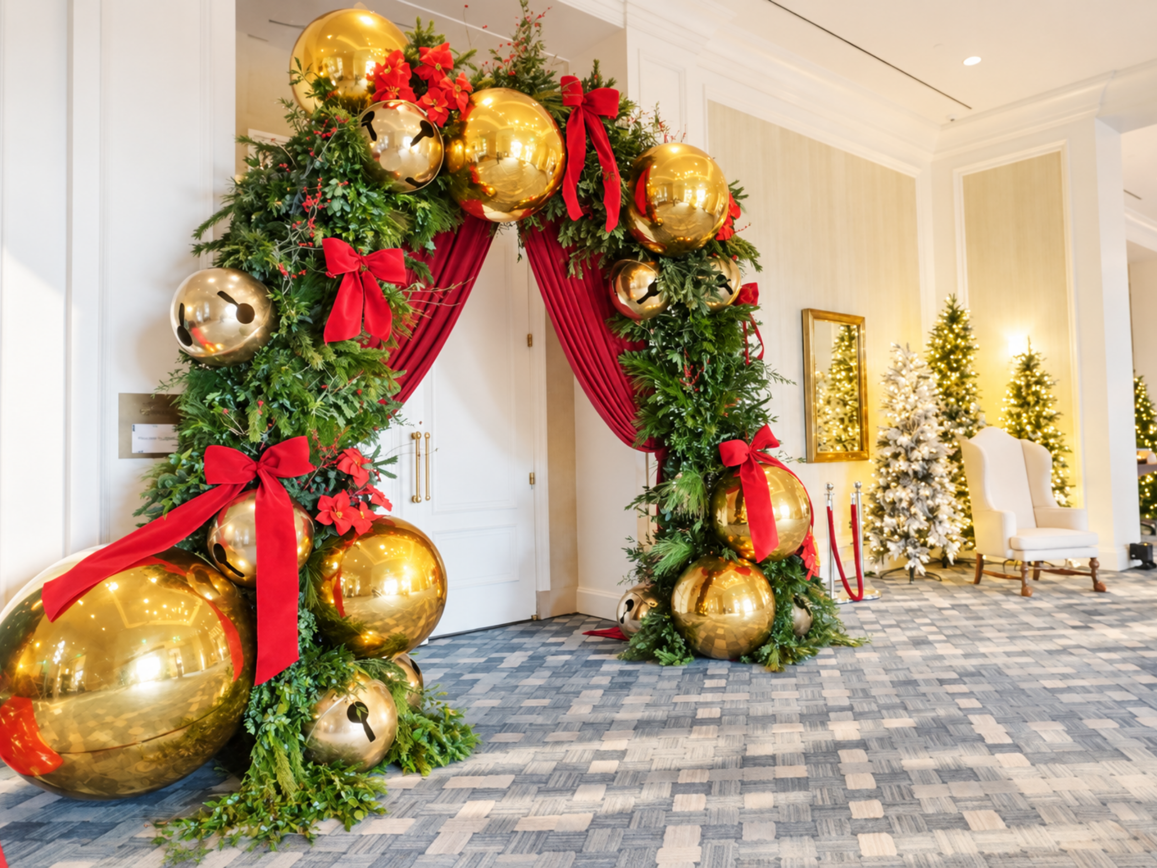 Festive Christmas event entrance in the Cayman Islands featuring an oversized greenery arch decorated with red bows and large gold ornaments, with illuminated Christmas trees in the background.