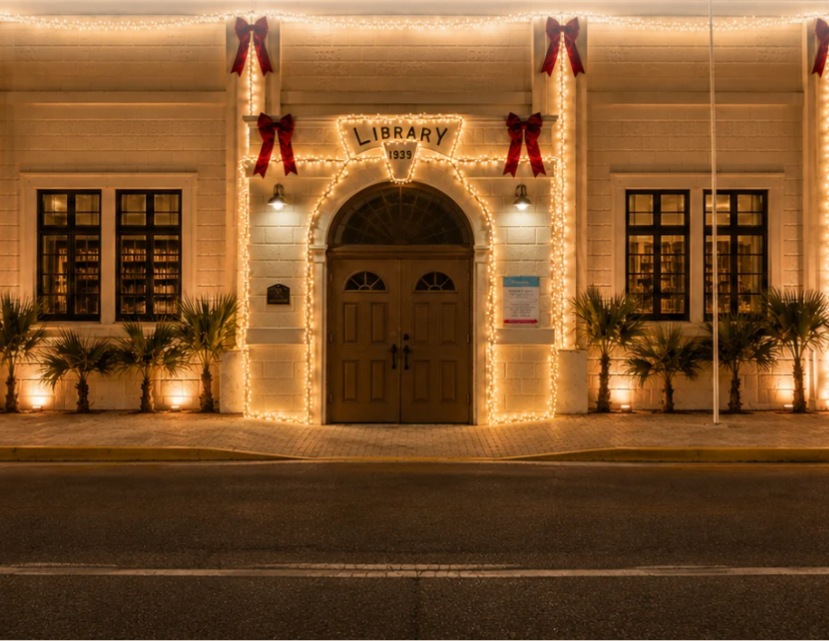 Warm white Christmas lights illuminate an elegant Cayman Islands home entrance, with festive red bows and greenery framing the doorway.